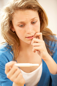 A worried looking young girl holding a pregnancy test.