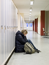 girl sitting alone against lockers looking sad.