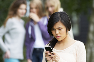 girl on phone while girls behind her whisper